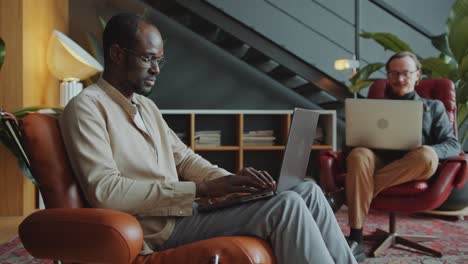 african american man sitting in armchair and working on laptop in office