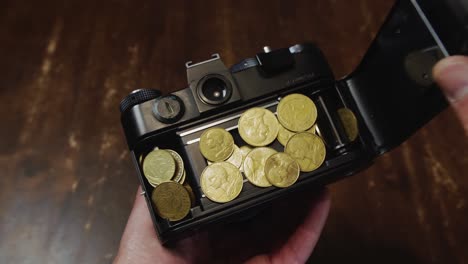 camera back opened by caucasian hand to reveal gold coins earned by the camera