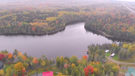 Toma-Aérea-De-Un-Impresionante-Lago-Con-Cabañas-Y-árboles-De-Colores-Otoñales-A-Su-Alrededor