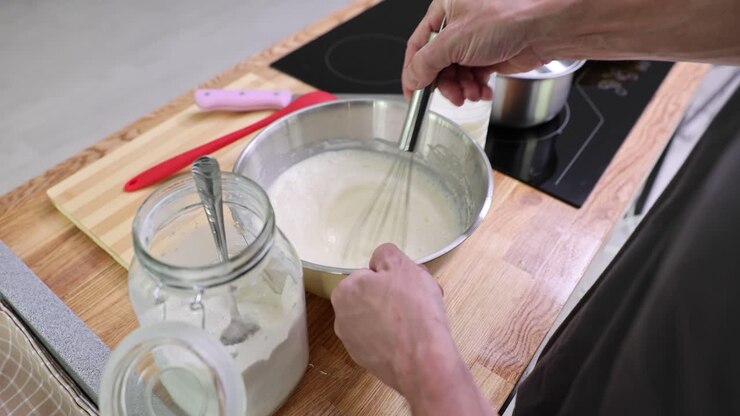 Hands whisking ingredients in a bowl while preparing food in a kitchen