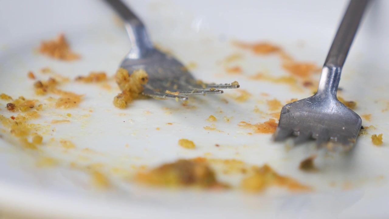 Dvě vidličky ležící na špinavém bílém talíři po jídle