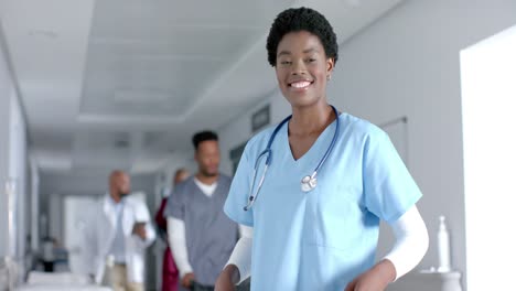 portrait of happy african american female doctor wearing scrubs, smiling in corridor, slow motion