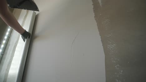 close-up view of a worker's arm installing a metal corner bead on a drywall to protect and define the edge of the plasterwork