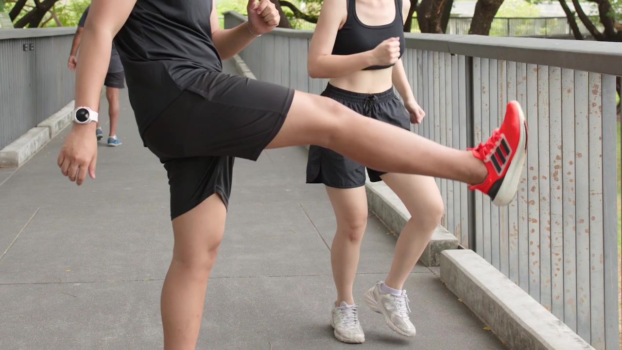 Uomo e donna thailandesi eseguono esercizi dinamici di stretching per le gambe su un ponte in un parco durante le ore diurne