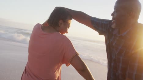 una pareja afroamericana de alto nivel sonriendo tomados de la mano y bailando en una playa soleada