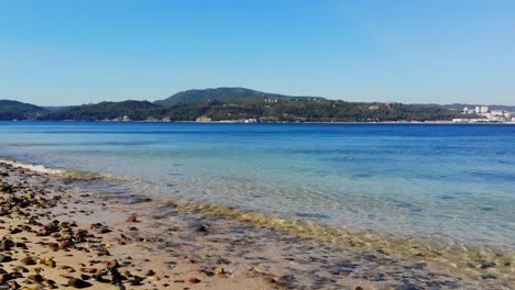 Calm-water-rolling-on-to-the-pebbles-on-a-small-beach,-with-lans-on-the-other-side