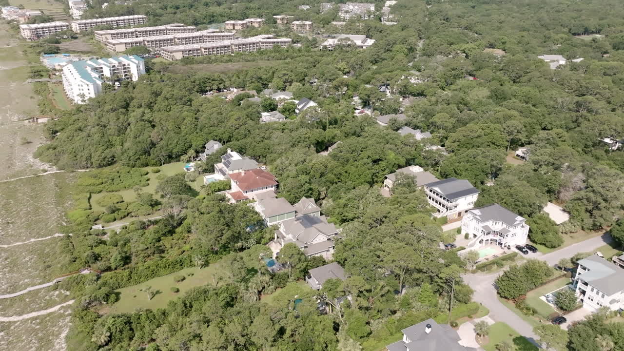 Aerial view of beachside homes nestled in dense trees, separated from the shoreline by dunes and narrow walkways