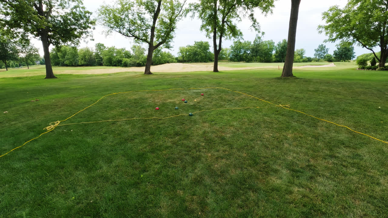 Shot of young caucasian female playing traditional boules game throwing heavy shiny red and green metal balls at target