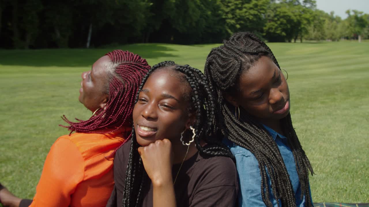 Joyful black family sitting back to back on lawn