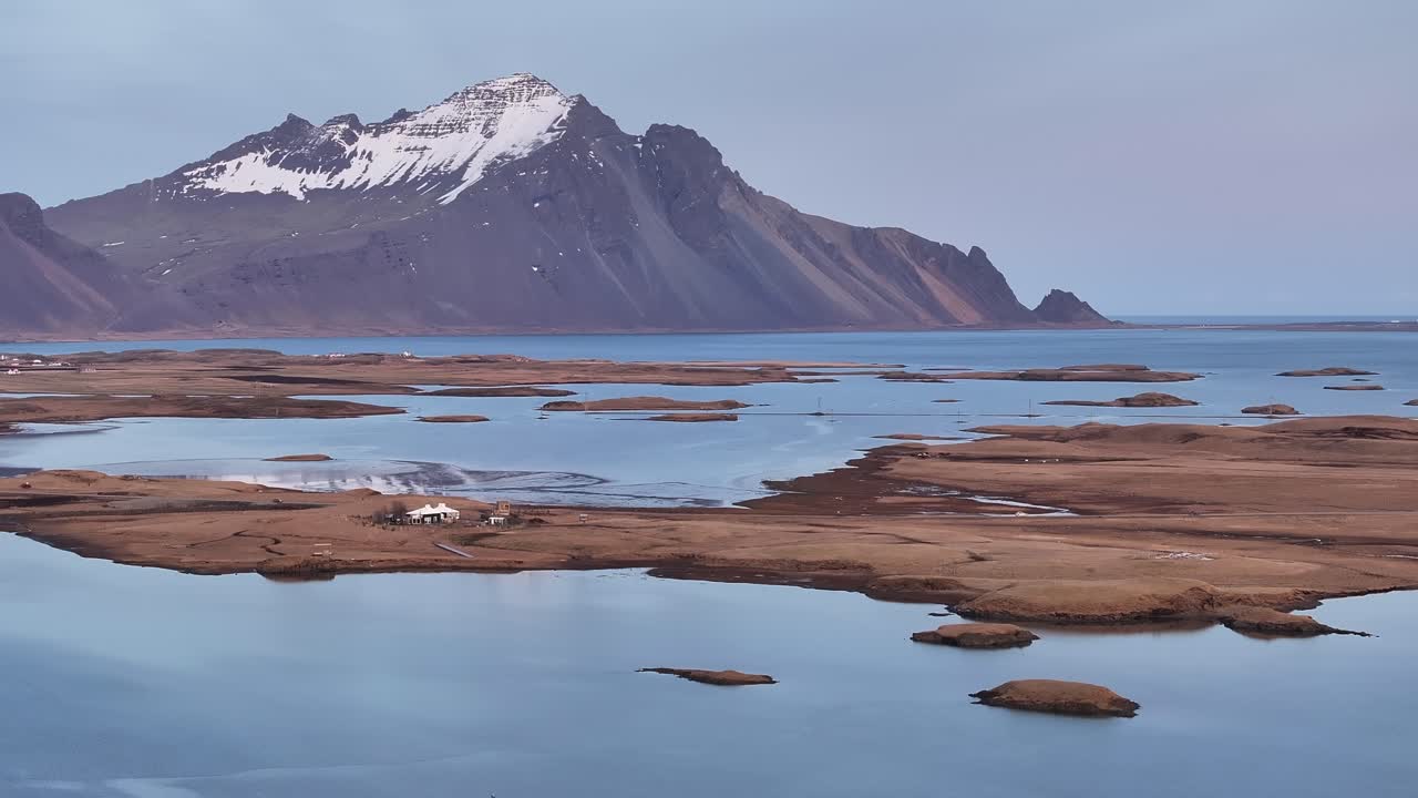 Farmstead in Hafnarnes, Höfn, with passing cars, Hornafjördur lagoon, and the Vatnajökull glacier towering in the background, Iceland.