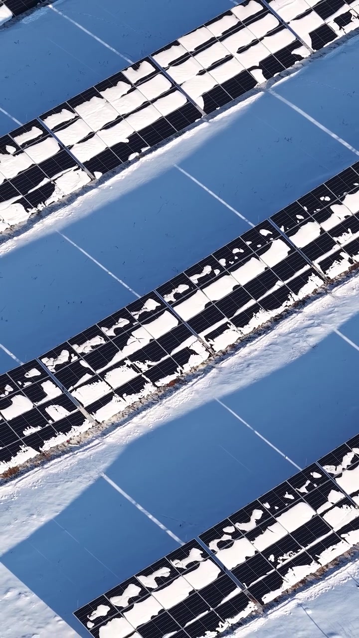 Ripresa aerea verticale che mostra pannelli solari coperti di neve in un impianto fotovoltaico, evidenziando la bassa produzione di energia in una fredda giornata invernale.