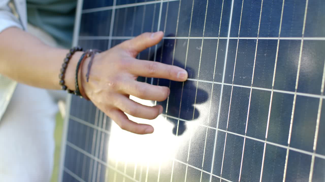 Una mano e un avambraccio si avvicinano al pannello solare da sinistra, toccando la griglia e ispezionandola sotto il sole