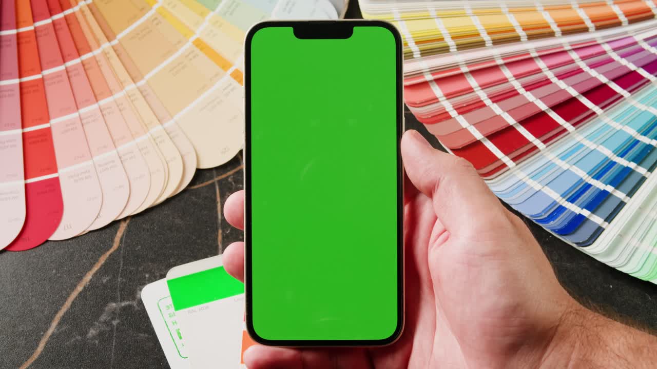 persona sosteniendo un teléfono inteligente con una pantalla verde contra un telón de fondo de muestras de pintura