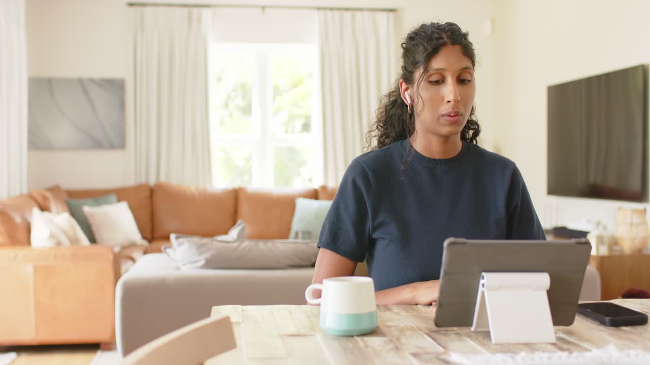 African woman raising palms signaling wait on call, leaning, tapping tablet at table in navy top