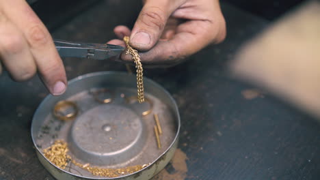 goldsmith cuts parts from shiny chain over metal box closeup