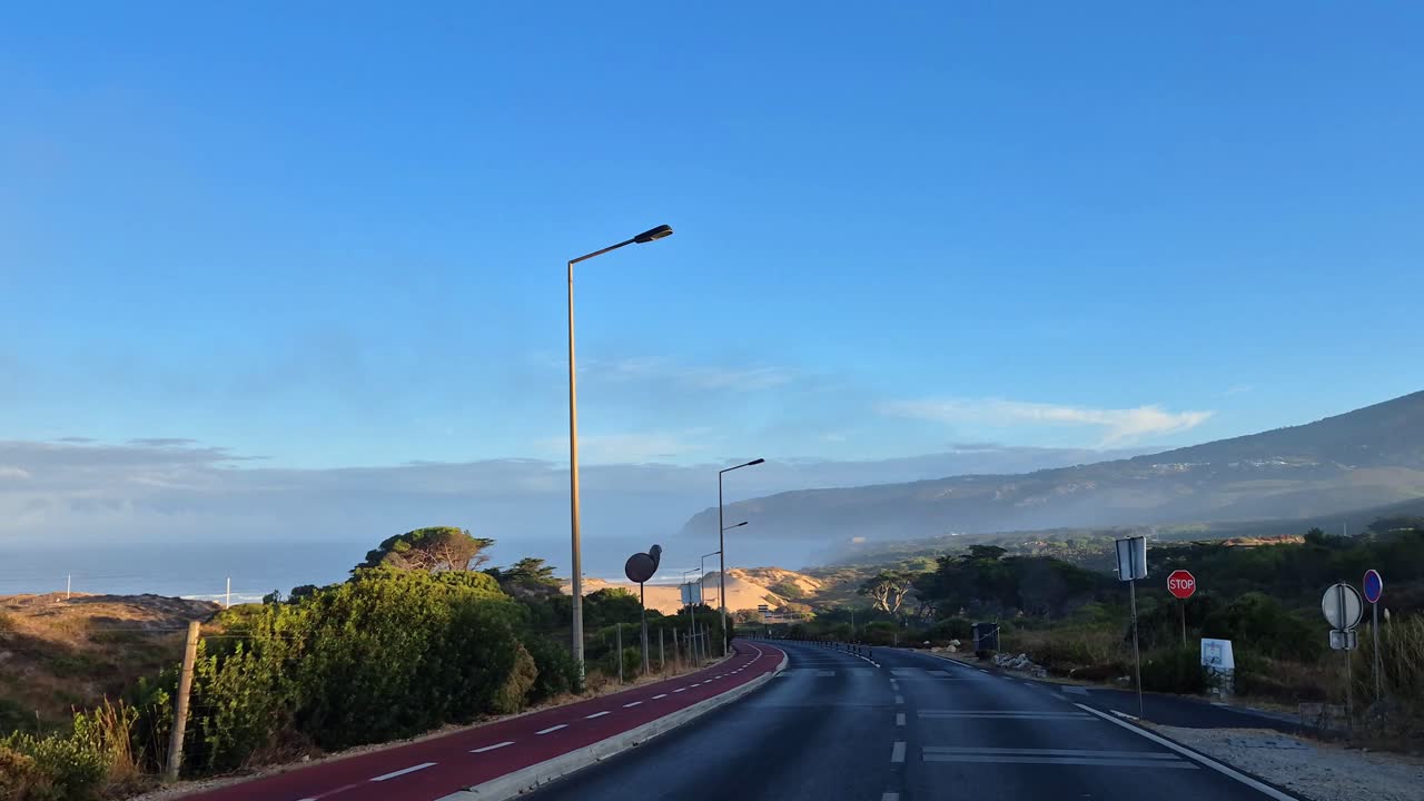 POV going down the road in the morning with the beautiful Guincho beach in the background and windy clouds,Cascais,Portugal