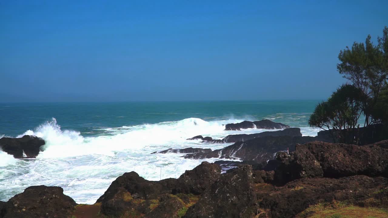 Slow motion of static shot rocky beach with powerful sea waves and blue sky - Menganti Beach, Indonesia
