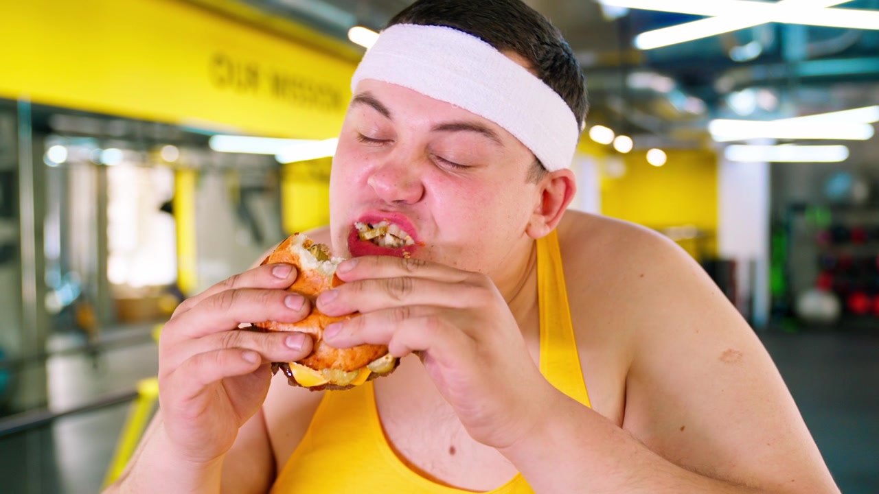 Uomo in sovrappeso che si concede un hamburger in palestra