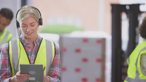 Gerente-Femenina-Usando-Auriculares-En-El-Almacén-De-Distribución-Logística-Usando-Tableta-Digital