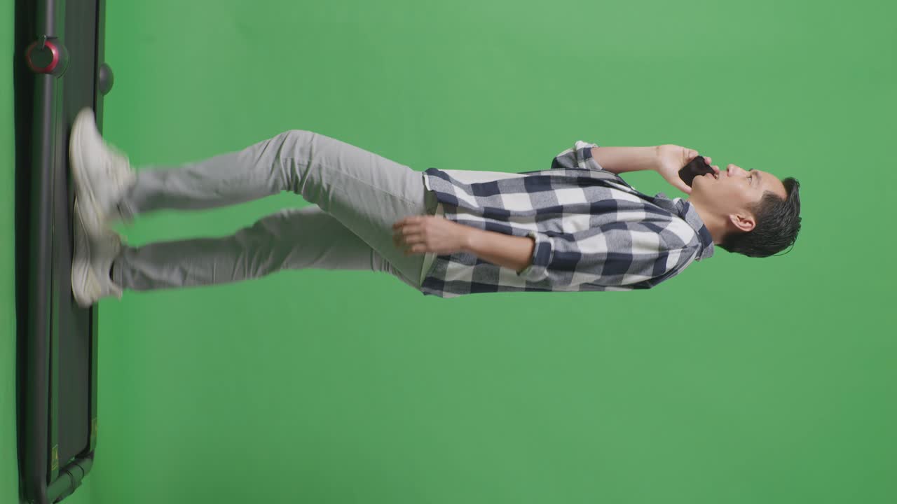 스튜디오에서 녹색 화면에서 는 동안 휴대 전화로 이야기하는 아시아 남자의 전체 몸의 측면 뷰