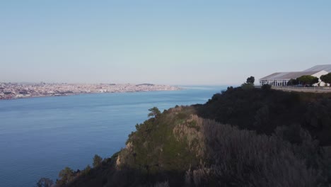 Drone-Volando-Sobre-El-Tejo-Hacia-El-Hermoso-Horizonte-De-Lisboa-Portugal-En-Un-Día-Soleado-En-Invierno