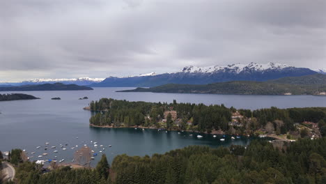 stunning aerial view of puerto manzano in villa la angostura, neuquén, argentina, with anchored boats and the majestic lake nahuel huapi as backdrop, surrounded by snow-capped mountains.