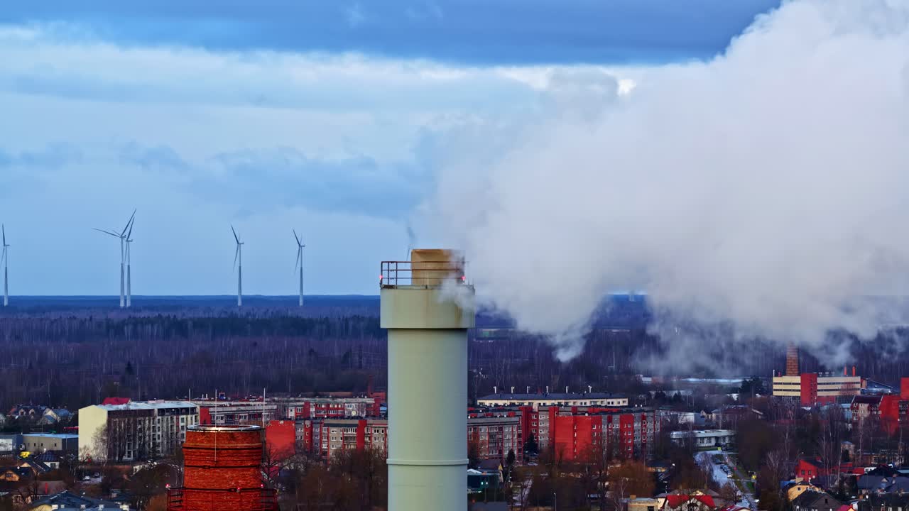 Drone in orbita attorno a un'alta ciminiera industriale con vapore e turbine eoliche