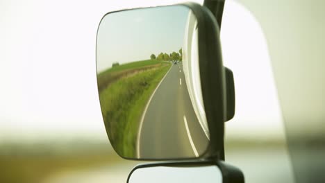 rear-view mirror reflecting a sunny rural road with cars in the distance, blurred vehicle edge