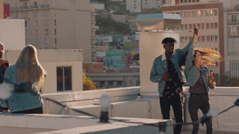 group of diverse friends hanging out dancing together enjoying rooftop party at sunset drinking alcohol having fun on weekend celebration