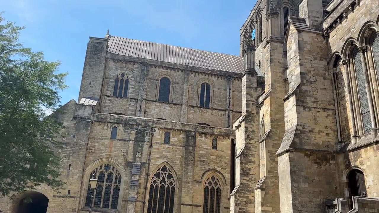 Inquadratura dal basso della Cattedrale di Winchester che rivela l'architettura gotica in pietra, la facciata storica e la torre medievale sotto un cielo azzurro e limpido a Winchester, Hampshire, Inghilterra
