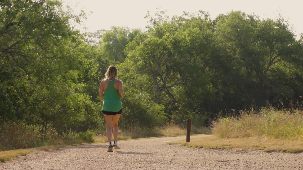A slow-motion shot captures a woman running gracefully on a scenic trail, highlighting her movement and the beauty of the surrounding nature as she embraces the outdoors.