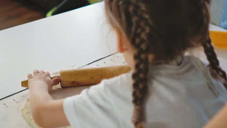 daughter-with-pigtails-rolls-out-yeast-dough-on-substrate