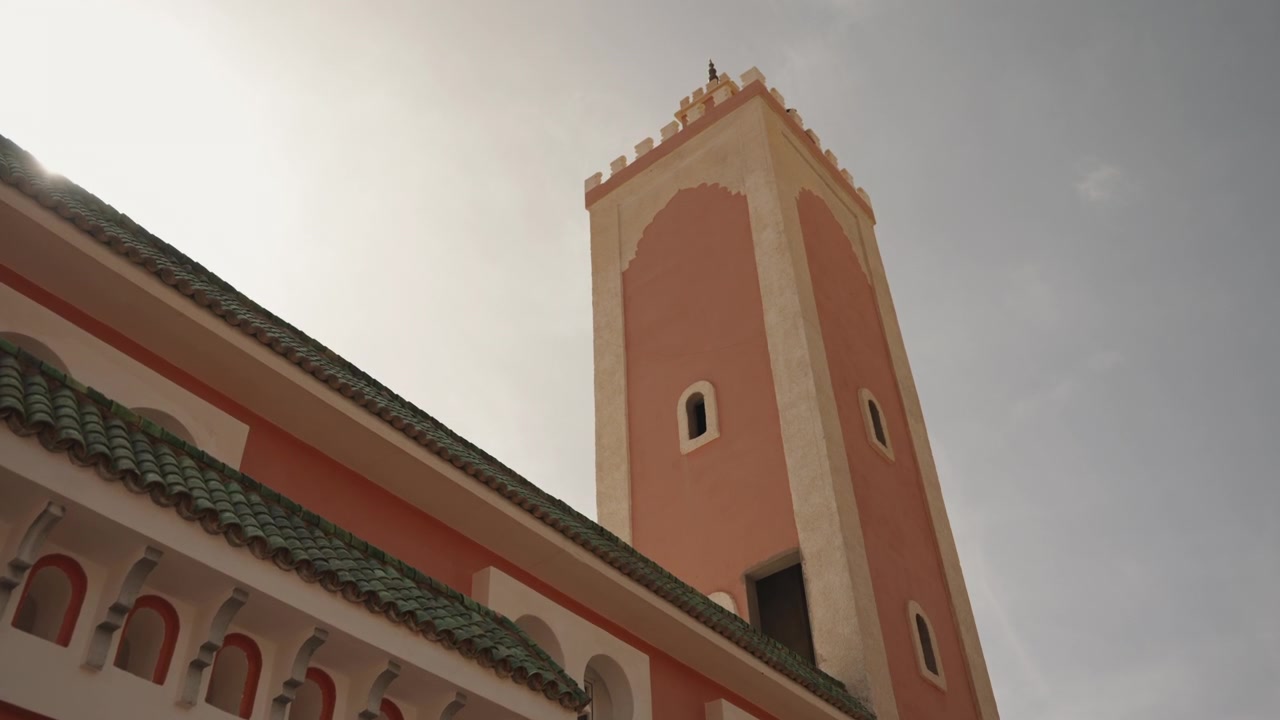 Minareto in intonaco rosa e tetto in tegole verdi di una moschea marocchina sotto un cielo pallido e velato