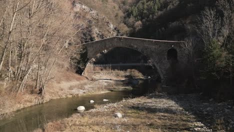 Steinbrücke-Umgeben-Von-Bäumen-Und-Wasser-Mit-Fahrzeugen-In-Der-Ferne