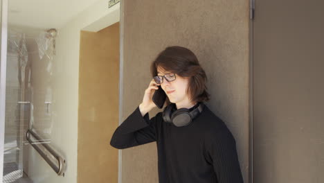 joven con gafas, auriculares alrededor del cuello, hablando en su teléfono móvil