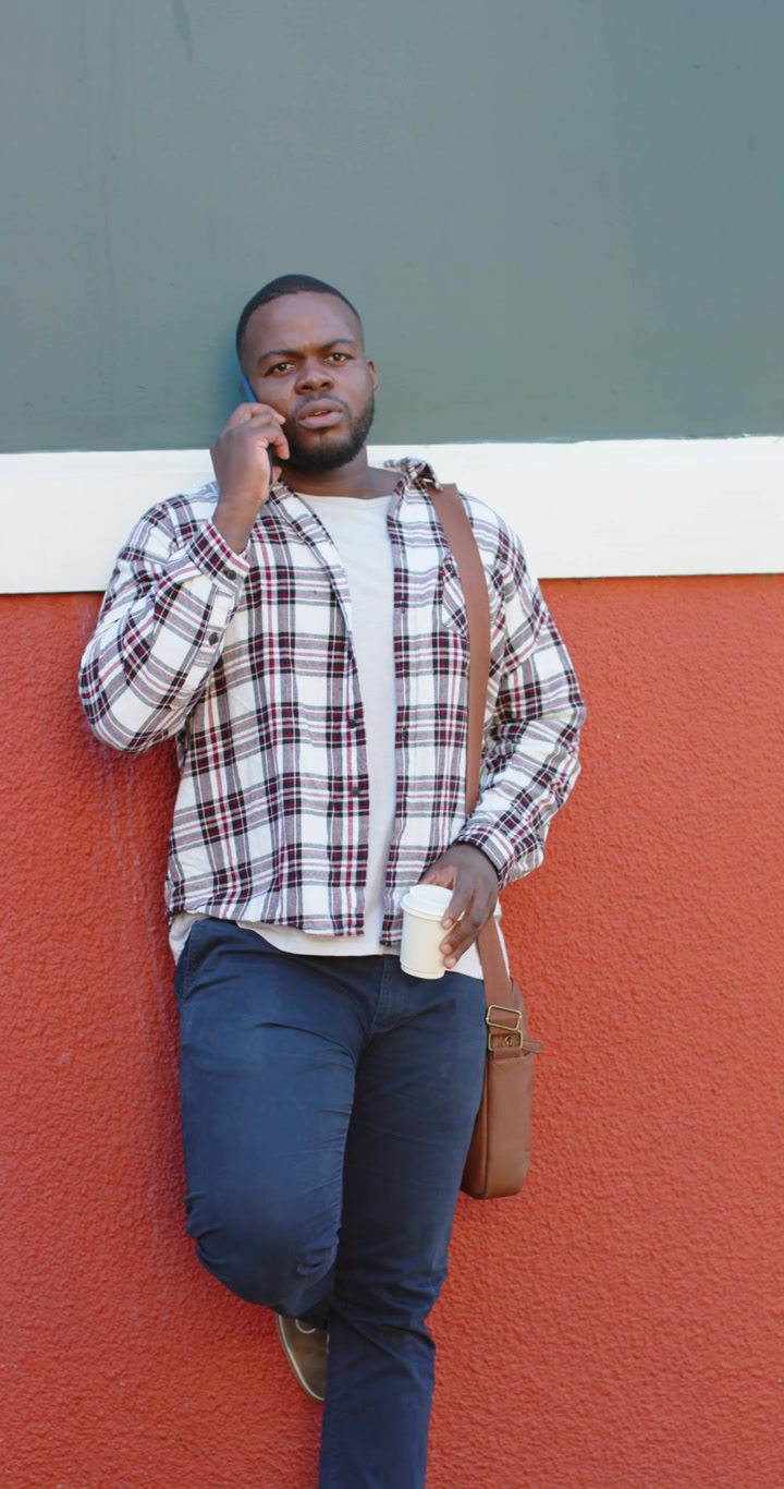 Vertical video: African American man answering phone call on sidewalk while sipping coffee