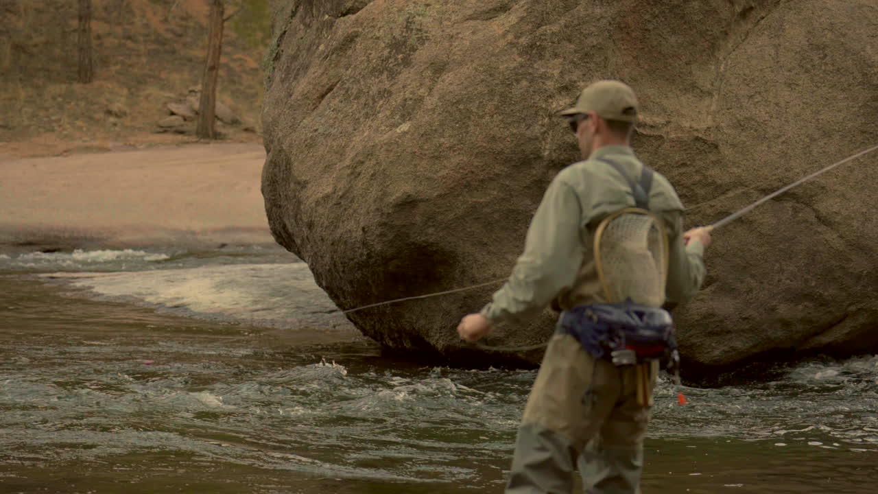 profundidad cinematográfica del campo río colorado pez mosca pescador con waders usando la caña de pesca en el agua por roca de roca cheesman cañón deckers coníferas perennes finales del invierno principios de la primavera sombra de la montaña