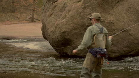 Cinematic-depth-of-field-Colorado-river-fly-fish-fisherman-with-waders-using-rod-fishing-in-water-by-boulder-rock-Cheesman-Canyon-Deckers-Conifer-Evergreen-late-winter-early-spring-shaded-mountainside
