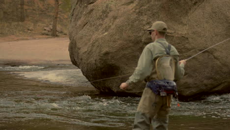 Filmische-Tiefenschärfe,-Colorado-River,-Fliegenfischen,-Fischer-Mit-Watvögeln,-Die-Angelrute-Im-Wasser-Verwenden,-Von-Felsbrocken,-Felsen,-Cheesman,-Canyondecker,-Nadelbaum,-Immergrün,-Spätwinter,-Vorfrühling,-Schattiger-Berghang