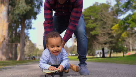 niño acostado en patineta, rodando hacia la cámara con la ayuda de su padre