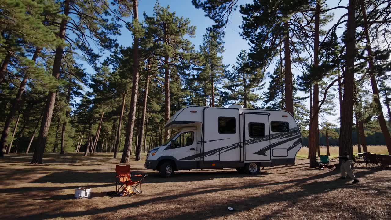 Wide-angle video shot of an RV parked in a serene forest setting, capturing tall pine trees
