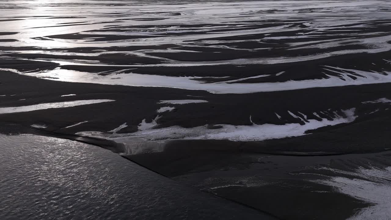 Dramatic aerial drone shot of a river winding through volcanic terrain in Iceland, with intertwining flows creating a poetic natural pattern