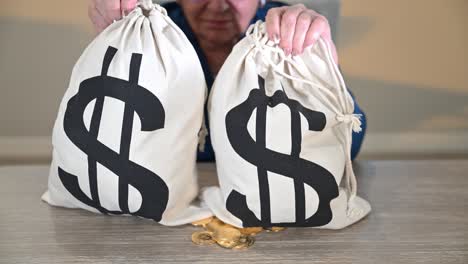 elderly woman lifting two money bags and dropping them on the table in front of gold souvenir bitcoins