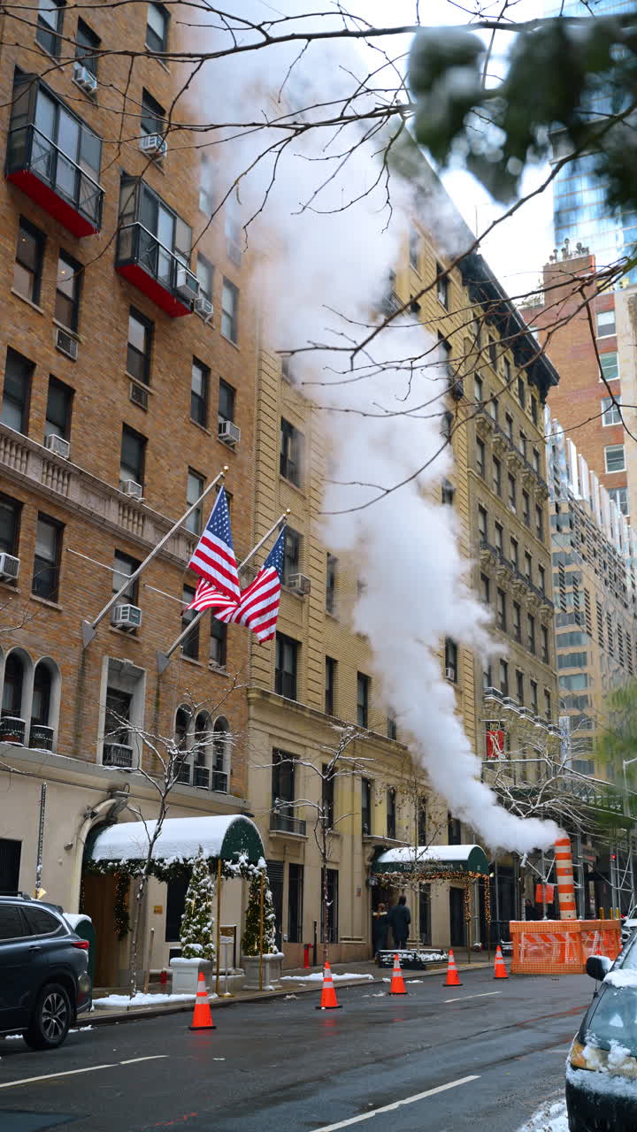 New York, USA, 24 dicembre 2025: bandiere americane su una strada innevata di Manhattan. Bandiere americane appese a un classico edificio di Manhattan con neve e vapore invernale sullo sfondo