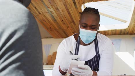 African-american-man-wearing-face-mask-taking-order-from-a-man-at-the-food-truck