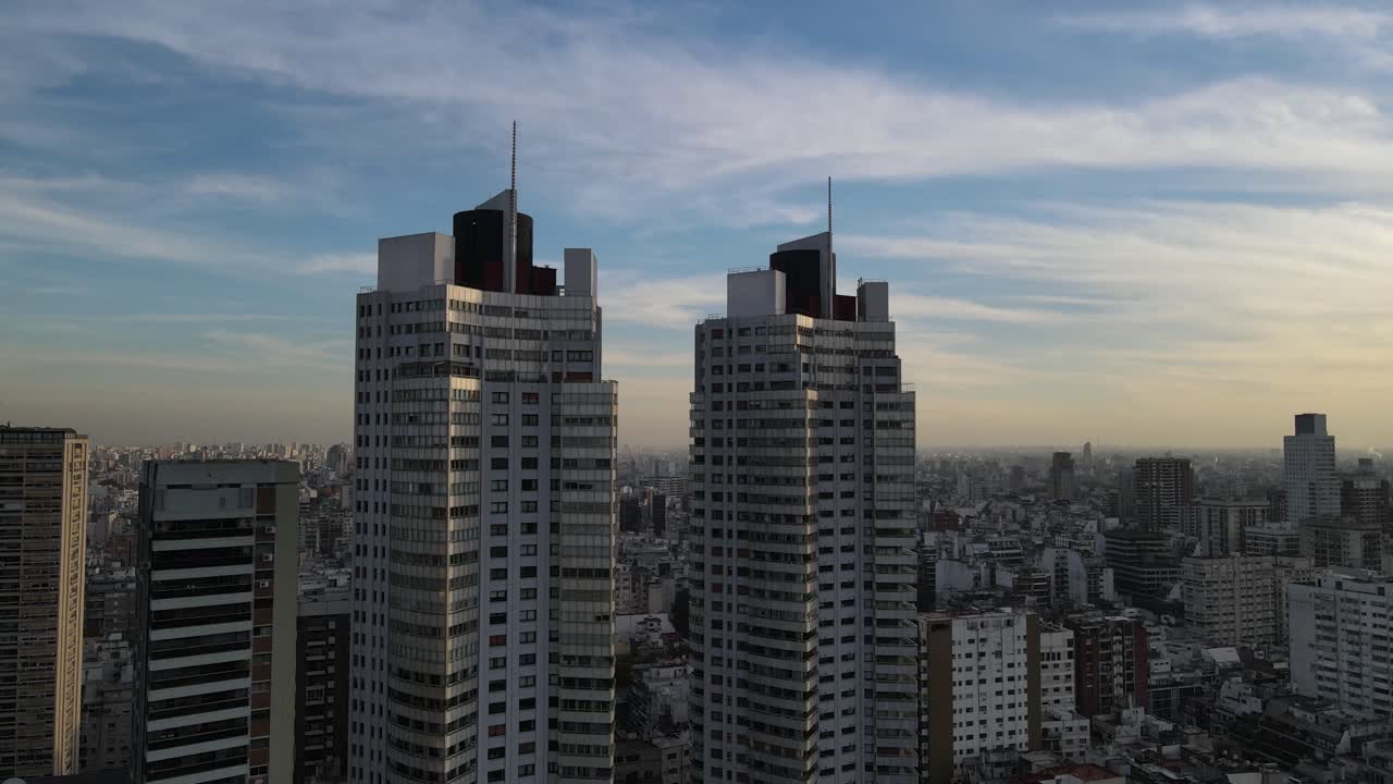 Aerial oribiting shot around two similar twin skyscraper in downtown of Buenos Aires during golden sunset.