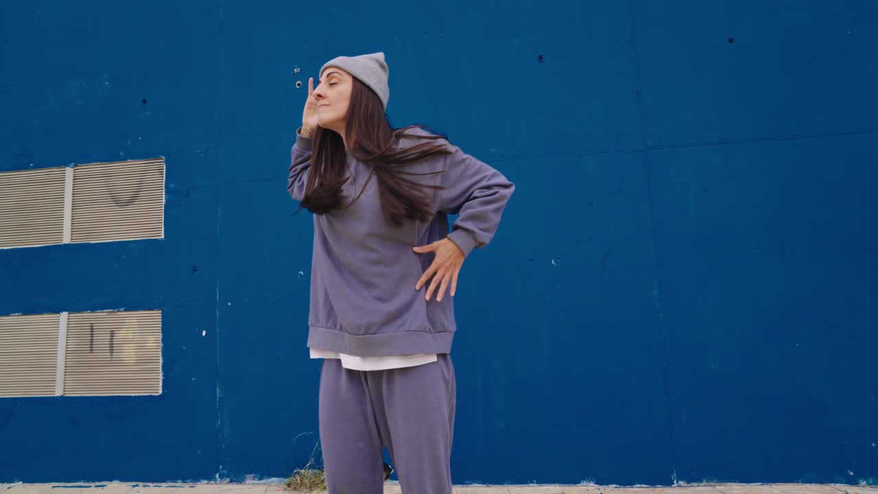Woman in street style dancing against a blue wall