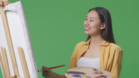 초록색 스크린 스튜디오에서 기둥 위에 그림을 그리는 여자