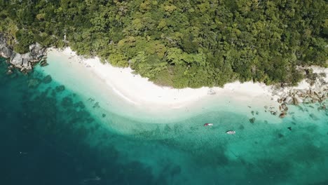 Drone-aerial-goes-down-and-spins-with-boats-in-tropical-blue-clear-water-and-rocks