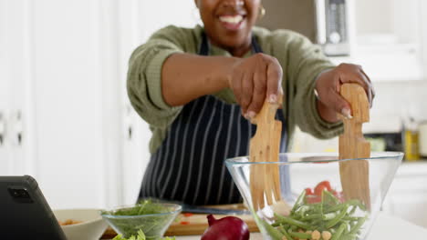 happy african american senior woman mixing vegetables and smiling in sunny kitchen, slow motion